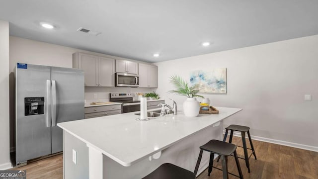 kitchen with appliances with stainless steel finishes, sink, gray cabinets, a center island with sink, and a breakfast bar area