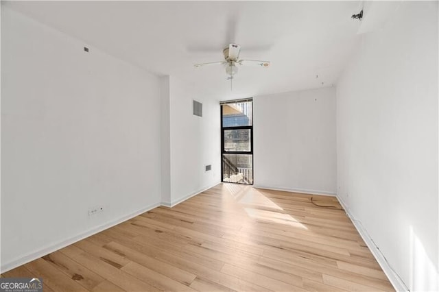 empty room with light wood-style floors, a wall of windows, baseboards, and a ceiling fan