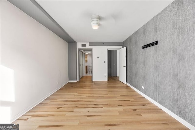 unfurnished bedroom with baseboards, an accent wall, visible vents, and light wood-style floors