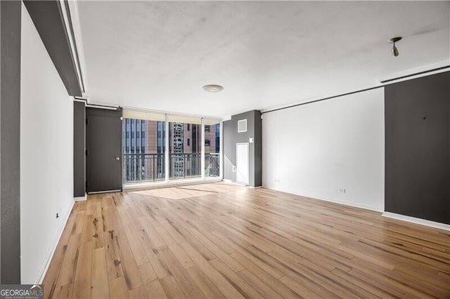 unfurnished room featuring expansive windows, baseboards, and light wood-style floors