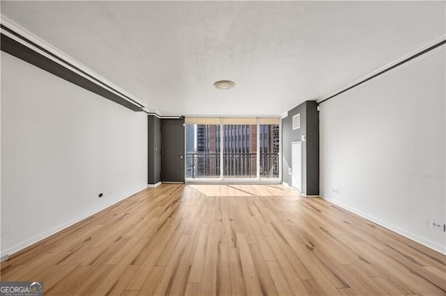 unfurnished living room featuring a wall of windows, light wood-type flooring, and baseboards