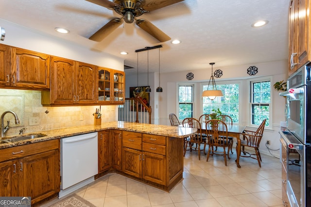 kitchen with pendant lighting, white refrigerator with ice dispenser, sink, kitchen peninsula, and light stone counters