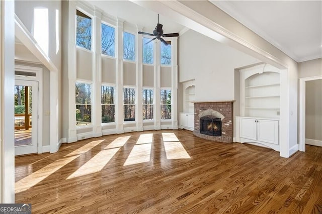 unfurnished living room featuring ceiling fan, hardwood / wood-style floors, a fireplace, ornamental molding, and built in shelves