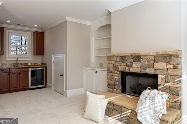 carpeted living room featuring a stone fireplace, built in features, sink, beverage cooler, and crown molding