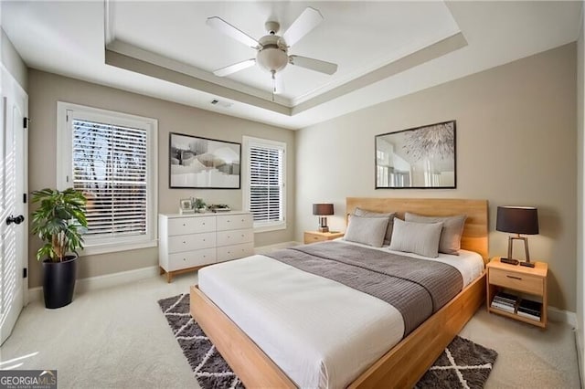 bedroom with ceiling fan, light colored carpet, and a raised ceiling