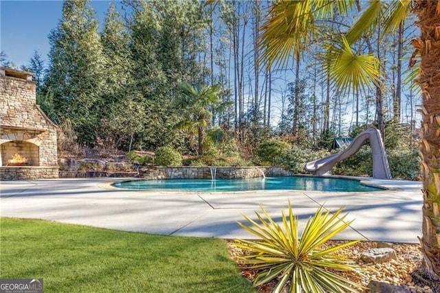 view of pool featuring a patio area, pool water feature, an outdoor stone fireplace, and a water slide