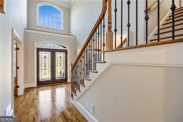 entryway with hardwood / wood-style flooring, ornamental molding, a towering ceiling, and french doors