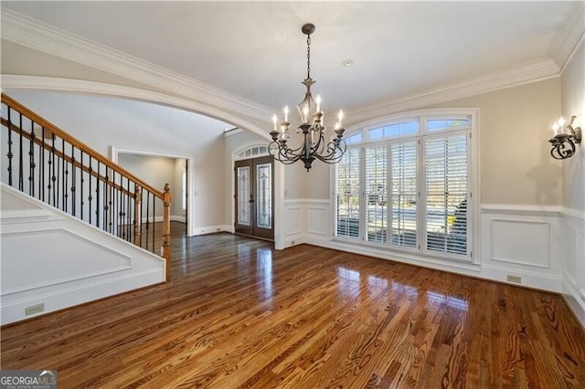 unfurnished dining area with crown molding, dark hardwood / wood-style floors, an inviting chandelier, and french doors