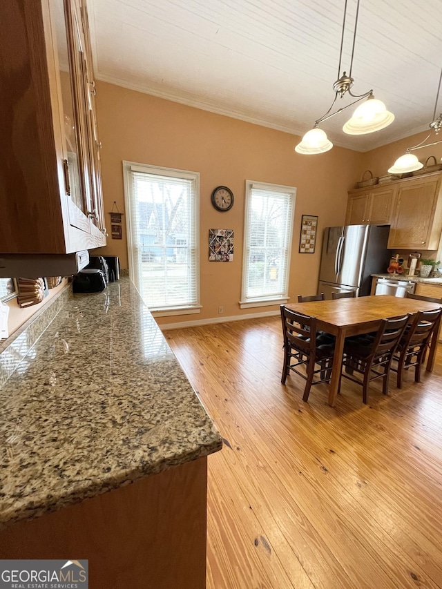 kitchen featuring decorative light fixtures, dark stone countertops, light hardwood / wood-style flooring, ornamental molding, and stainless steel appliances