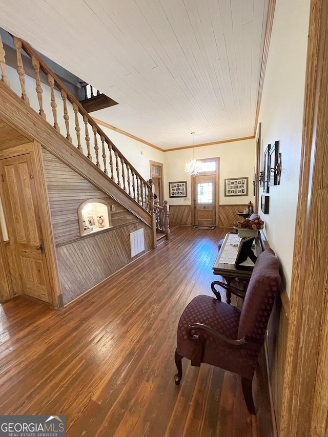 sitting room with wood ceiling, wood-type flooring, wood walls, a notable chandelier, and crown molding