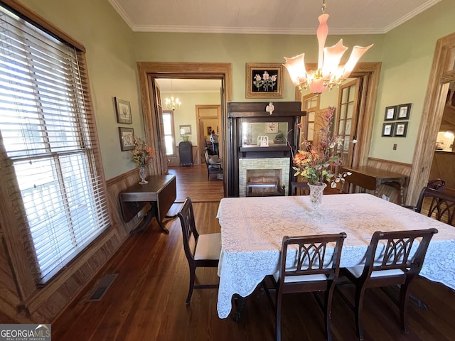 dining room with dark hardwood / wood-style flooring, a stone fireplace, wood walls, a chandelier, and crown molding