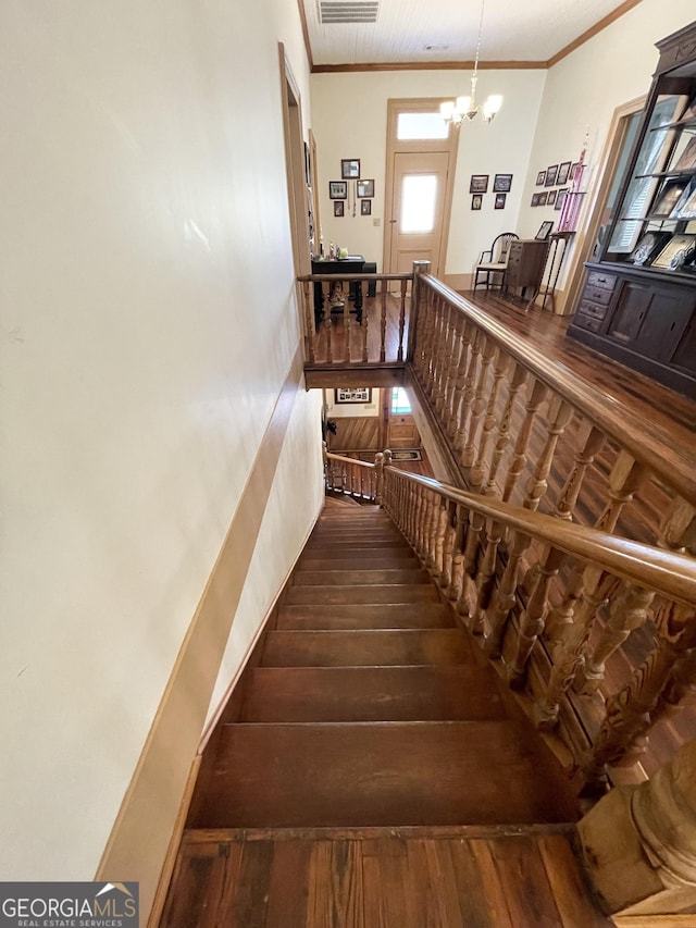 stairway featuring wood-type flooring, crown molding, and a notable chandelier