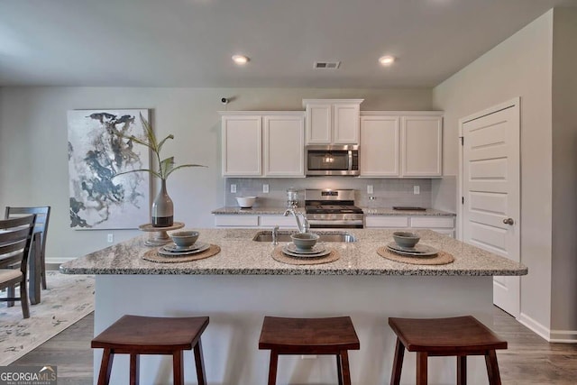 kitchen with dark hardwood / wood-style floors, white cabinets, appliances with stainless steel finishes, and a center island with sink