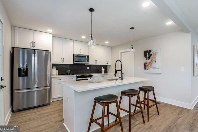 kitchen featuring stainless steel appliances, white cabinetry, decorative light fixtures, and a kitchen island with sink