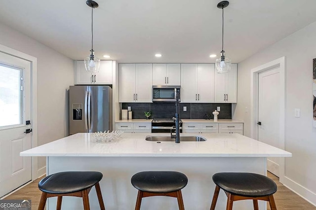 kitchen with white cabinetry, stainless steel appliances, sink, hanging light fixtures, and a kitchen island with sink