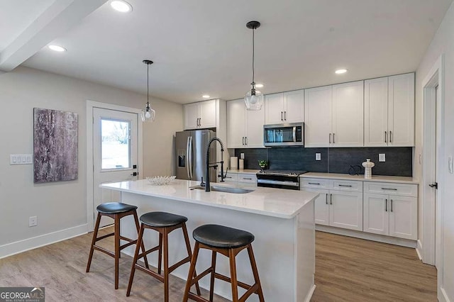 kitchen with sink, light wood-type flooring, appliances with stainless steel finishes, an island with sink, and white cabinets