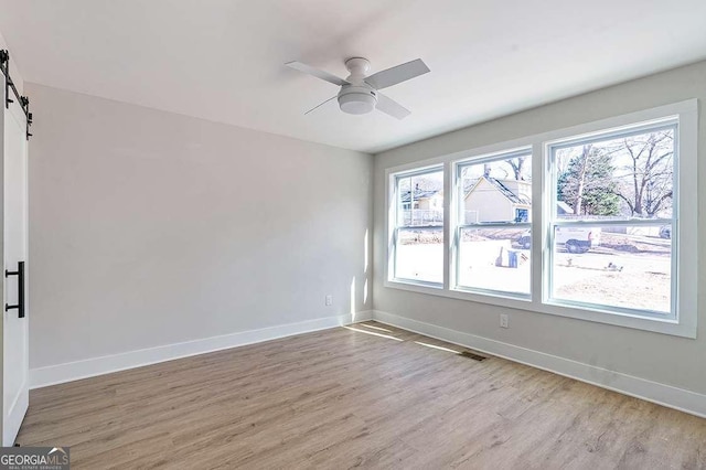 spare room featuring ceiling fan, light hardwood / wood-style floors, and a barn door