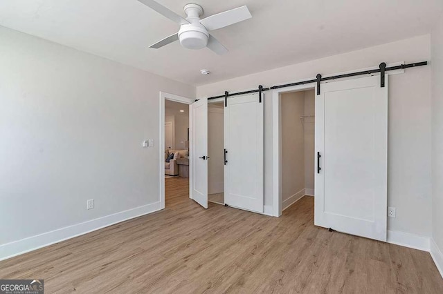 unfurnished bedroom featuring ceiling fan, a barn door, light hardwood / wood-style flooring, a walk in closet, and a closet