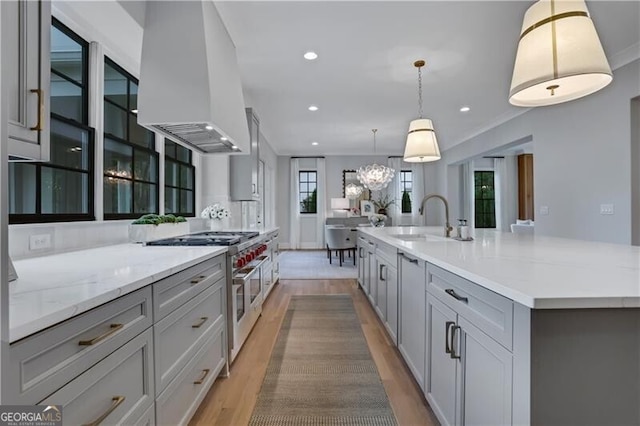 kitchen featuring a spacious island, decorative light fixtures, double oven range, sink, and range hood