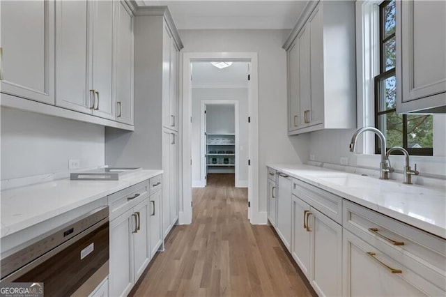 kitchen featuring dishwasher, sink, light hardwood / wood-style flooring, ornamental molding, and light stone counters