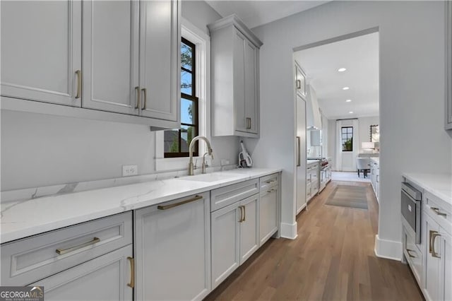 kitchen with light stone countertops, dark hardwood / wood-style flooring, sink, gray cabinets, and stainless steel microwave