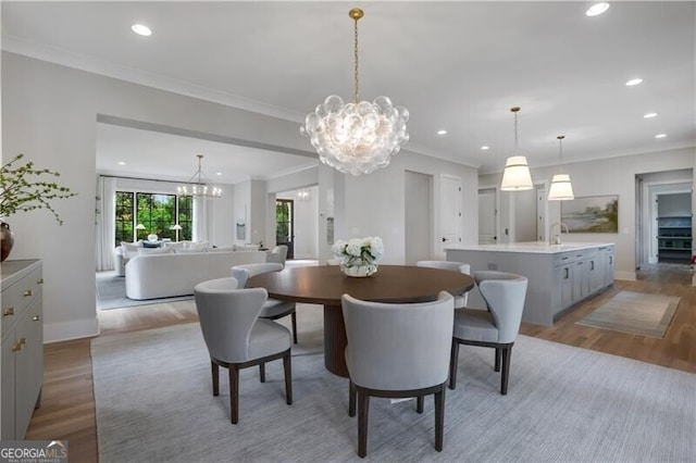 dining area with light wood-type flooring, a notable chandelier, sink, and ornamental molding