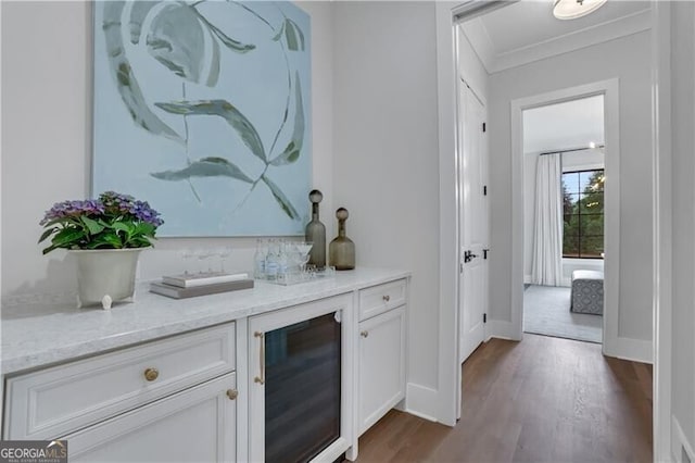 bar with light stone countertops, dark wood-type flooring, white cabinetry, wine cooler, and ornamental molding