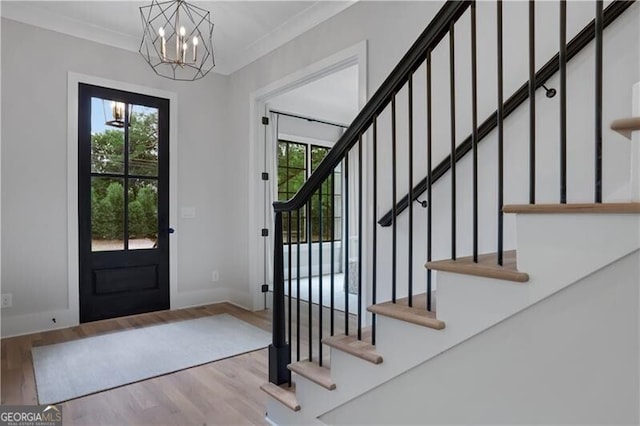 entryway with light wood-type flooring, an inviting chandelier, a wealth of natural light, and ornamental molding