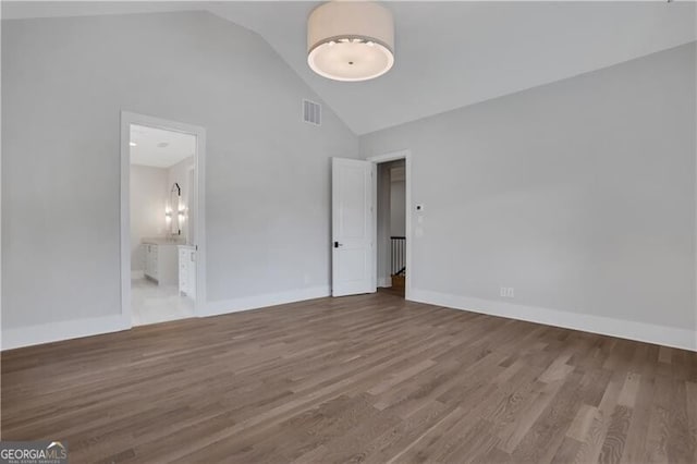 unfurnished bedroom featuring high vaulted ceiling, wood-type flooring, and ensuite bath