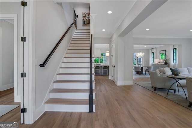 stairs with wood-type flooring, crown molding, and a notable chandelier