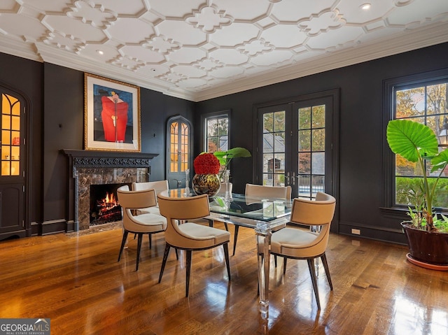 dining space featuring wood-type flooring, ornamental molding, french doors, and a fireplace