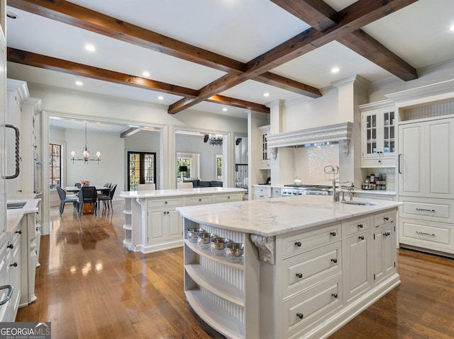 kitchen with sink, an inviting chandelier, an island with sink, white cabinets, and light stone counters