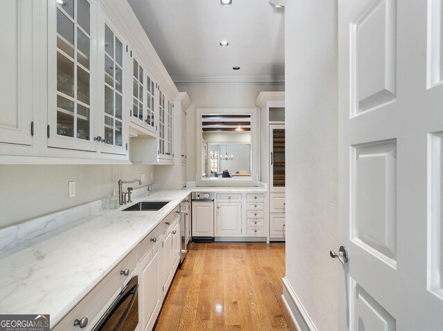 kitchen featuring white cabinetry, light stone countertops, crown molding, light hardwood / wood-style flooring, and sink