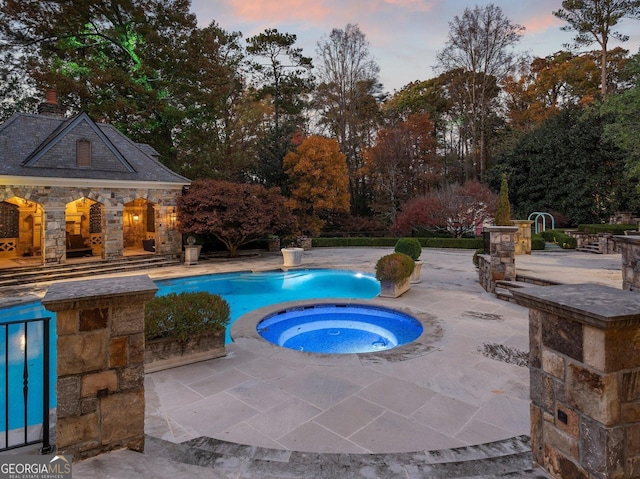 pool at dusk with an in ground hot tub and a patio