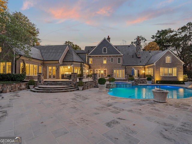 pool at dusk featuring an in ground hot tub and a patio