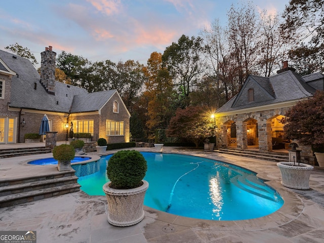 pool at dusk with an in ground hot tub and a patio