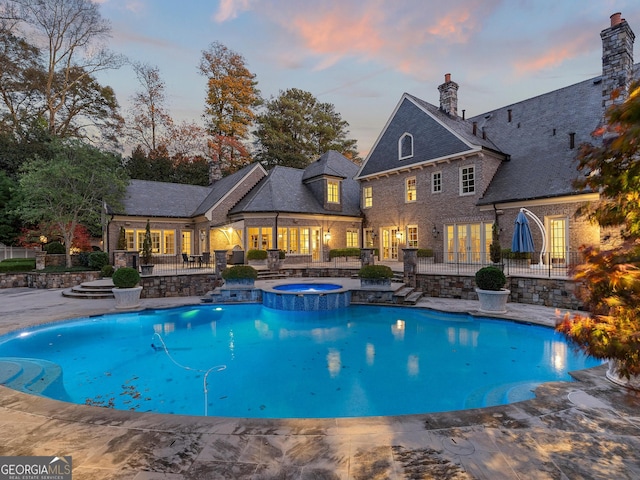 pool at dusk with a patio area and an in ground hot tub