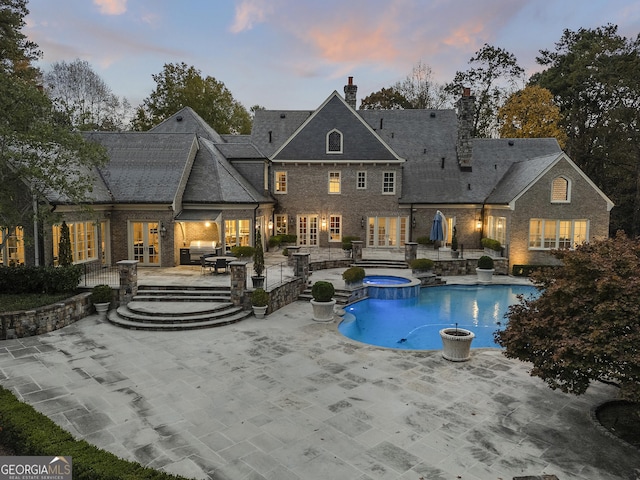 back house at dusk with a pool with hot tub and a patio