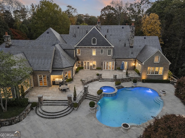 pool at dusk with an in ground hot tub, area for grilling, french doors, and a patio