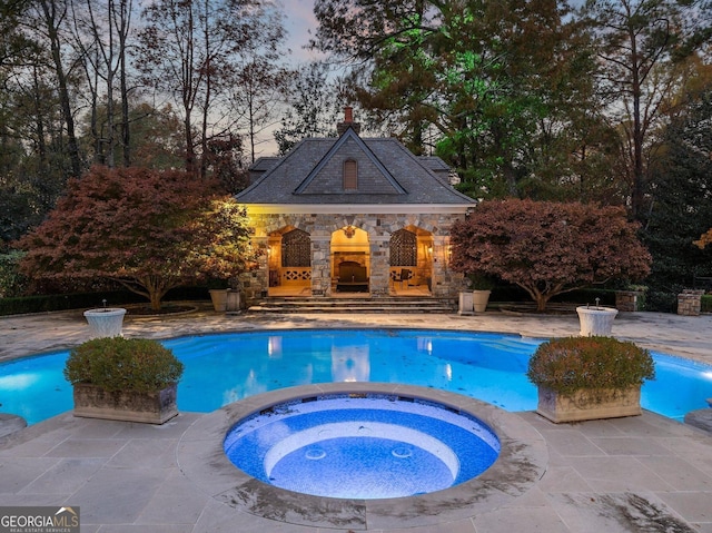 pool at dusk with a patio area, an in ground hot tub, and an outdoor stone fireplace