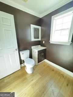 bathroom with toilet, vanity, wood-type flooring, and crown molding