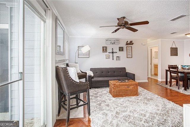 living room with ceiling fan, a textured ceiling, ornamental molding, and hardwood / wood-style flooring