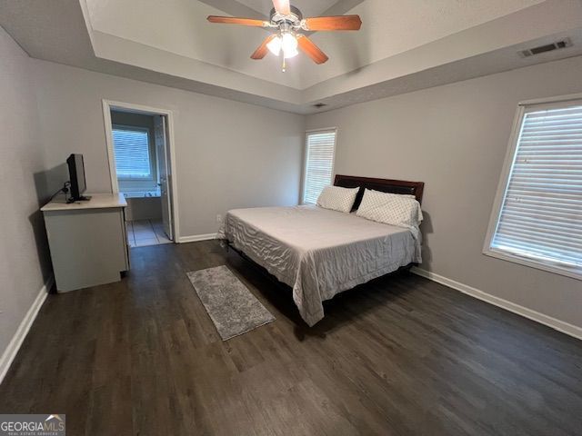 bedroom featuring ceiling fan, dark wood-type flooring, connected bathroom, and a tray ceiling