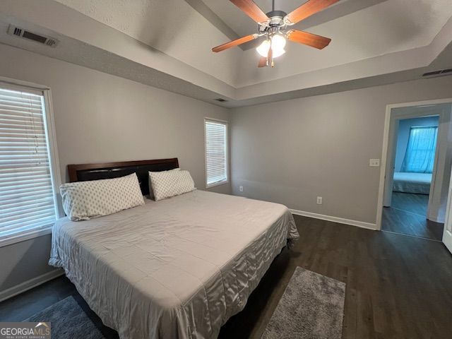 bedroom with dark wood-type flooring, ceiling fan, a raised ceiling, and multiple windows