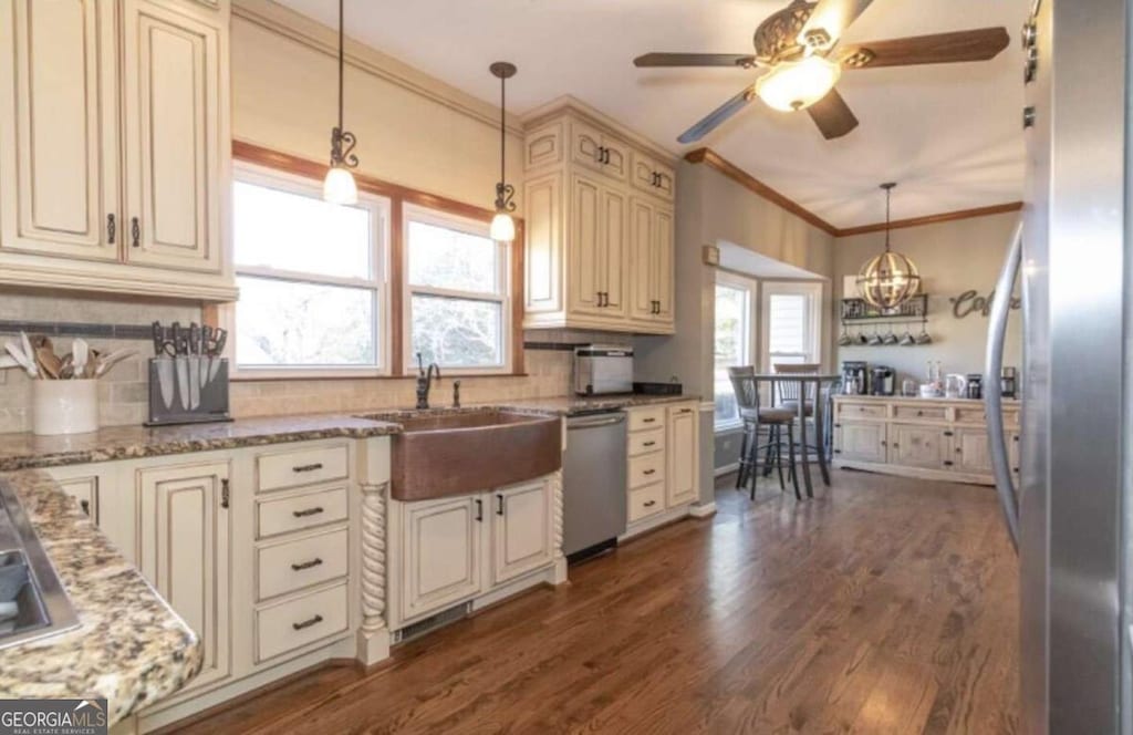 kitchen featuring light stone countertops, appliances with stainless steel finishes, cream cabinetry, and decorative light fixtures