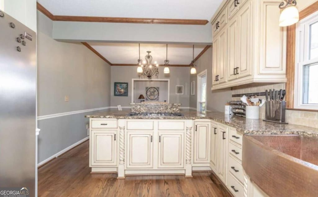 kitchen with an inviting chandelier, kitchen peninsula, appliances with stainless steel finishes, pendant lighting, and cream cabinets