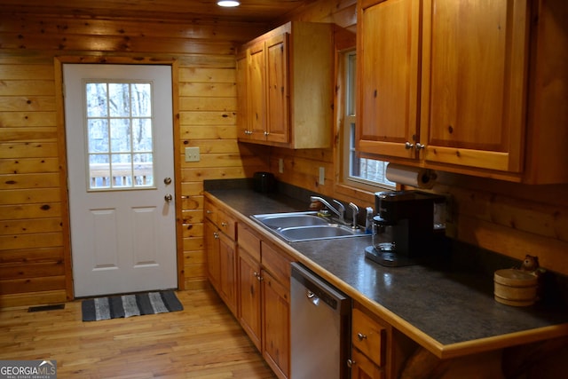 kitchen featuring a breakfast bar, wood walls, dishwasher, sink, and light wood-type flooring