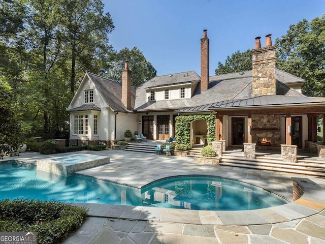 back of property featuring a patio, metal roof, an outdoor stone fireplace, french doors, and a standing seam roof