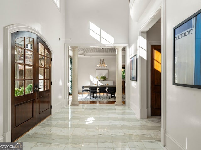 entryway with marble finish floor, french doors, a notable chandelier, a towering ceiling, and ornate columns