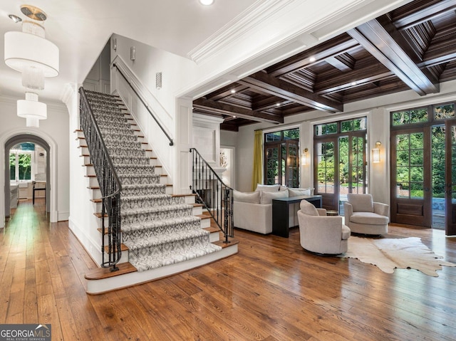 entryway featuring ornamental molding, arched walkways, wood-type flooring, and beamed ceiling